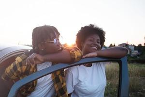 duas mulheres afro-americanas felizes perto do carro ao pôr do sol, estilo de vida