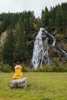 uma pessoa sentado em uma Rocha perto uma cascata foto