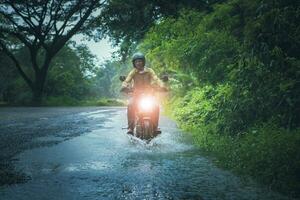 homem equitação pequeno enduro motocicleta cruzando raso Riacho entre chuva queda às floresta foto