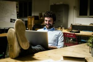 homem de negocios usando computador portátil dentro escritório com pés em escrivaninha foto