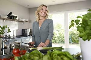 sorridente mulher corte Primavera cebolas dentro cozinha foto