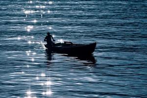 pequeno barco no lago em silhueta com reflexos dos raios solares foto