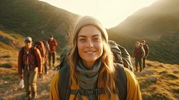 uma sorridente jovem mulher caminhante com mochila olhando às Câmera com grupo do amigos caminhantes sobe para a topo do a colina. caminhante, turista acampamento. generativo ai foto
