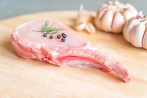 Costeleta de porco fresca na tábua de madeira com alho e pimenta preta foto