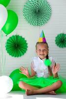 pequeno menina com uma boné em dela cabeça contra a fundo do verde balões. aniversário para crianças. foto