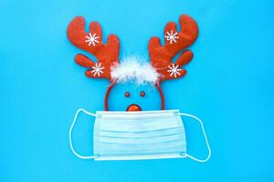 veado face fez a partir de uma veado chifre aro e uma Natal brinquedo dentro uma médico mascarar em uma azul fundo. foto
