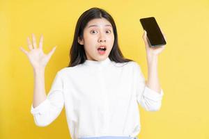 jovem asiática segurando um telefone com expressão em fundo amarelo foto