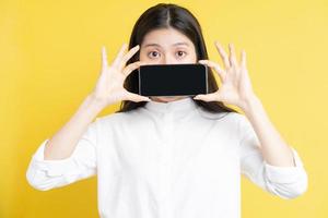 jovem asiática segurando um telefone com expressão em fundo amarelo foto