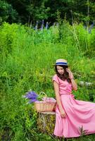lindo menina dentro uma lindo vestir senta em uma toco dentro a floresta, uma ramalhete do tremoço dentro uma cesta foto