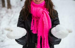 jovem mulher segurando natural suave branco neve dentro dela mãos para faço uma bola de neve, sorridente em uma frio inverno dia dentro a floresta, ao ar livre. foto