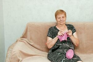 Senior mulher tricô sentado às casa em a sofá foto