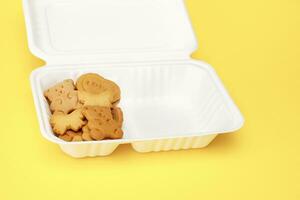 crianças biscoitos dentro a Formato do corações, ursos, borboletas dentro uma biodegradável descartável almoço caixa em uma amarelo fundo foto