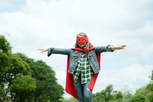 em uma lindo dia dentro a parque, uma jovem menina goza dela período de férias. brincalhão com uma vermelho Super heroi traje e mascarar. foto