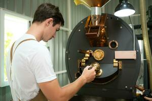 retrato do uma jovem homem trabalhando com uma café torrador máquina foto