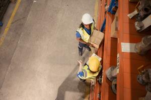 Alto ângulo Visão do armazém trabalhadores dentro capacetes elevação caixas às armazém foto