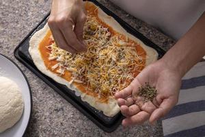 Mulher com as mãos adicionando orégano a uma pizza