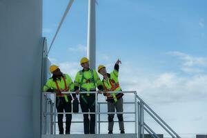 grupo do engenheiros e técnicos em pé em a escadas do uma vento turbina, a conceito do natural energia a partir de vento. foto