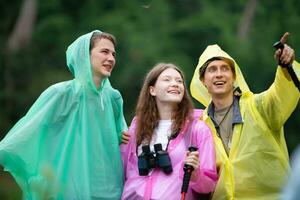 grupo do feliz amigos dentro capas de chuva e capas de chuva olhando às montanha e floresta depois de a chuva parou foto