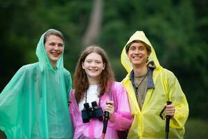 grupo do feliz amigos dentro capas de chuva e capas de chuva olhando às montanha e floresta depois de a chuva parou foto