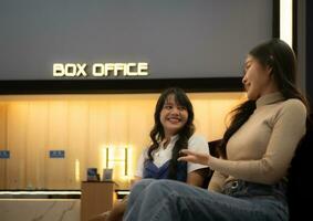 dois jovem ásia mulheres comendo Pipoca e esperando para assistindo filme às frente do caixa escritório foto