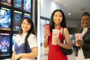 jovem ásia mulher em pé dentro linha para Comprar filme bilhetes e dentro mão Pipoca e beber foto