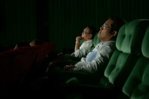 jovem casal assistindo filme dentro cinema, sentado em a verde assentos. foto