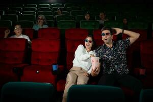 dentro uma cinema, uma jovem casal par vestindo 3d óculos relógios filmes e come Pipoca. foto