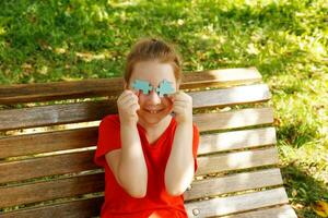 fofa sorridente menina dentro a parque em a Banco fechadas dela olhos com enigma elementos foto