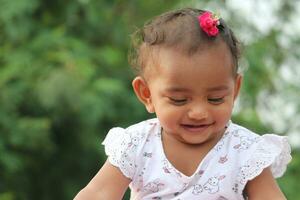 fofa tamil bebê menina sorrir dentro a parque com verde fundo foto