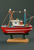 miniatura vermelho e branco pescaria barco modelo em cinzento fundo foto