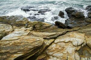 uma rochoso litoral com ondas falhando contra a pedras foto