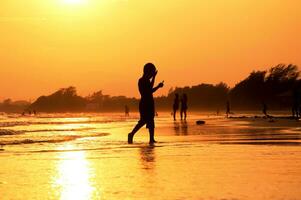 uma pessoa caminhando em a de praia às pôr do sol foto