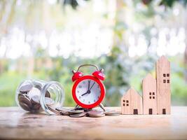 Tempo é dinheiro conceito. vermelho alarme com miniatura casa em pilha do moedas. a salvando conceito para casa e propriedade. foto