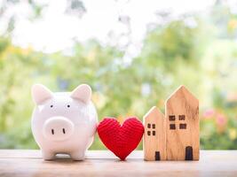 porquinho banco, vermelho coração e miniatura casa. a salvando conceito para casa e propriedade. foto