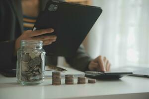 salvando dinheiro e contabilidade conceito. o negócio homem colocando moeda inserir para jarra e faço contabilidade livro para finança gestão para investimento e economizando. foto