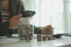 salvando dinheiro e contabilidade conceito. o negócio homem colocando moeda inserir para jarra e faço contabilidade livro para finança gestão para investimento e economizando. foto