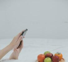 eficiente jovem milenar menina sentado em uma cama dentro a manhã, usa computador portátil computador e come croissants e bebidas café para café da manhã foto