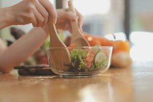 delicioso fruta e legumes em uma mesa e mulher culinária. dona de casa é corte verde pepinos em uma de madeira borda para fazer fresco salada dentro a cozinha. foto