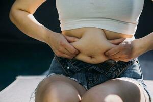 mulher gorda, barriga gorda, gordinha, mão de mulher obesa segurando gordura excessiva da barriga com fita métrica, conceito de estilo de vida de dieta de mulher foto