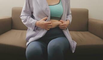 uma mulher mostra a inflado Grosso barriga, a conceito do excesso peso e peso perda foto
