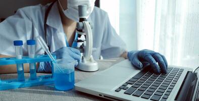 jovem cientistas conduzindo pesquisa investigações dentro uma médico laboratório, uma investigador dentro a primeiro plano é usando uma microscópio foto