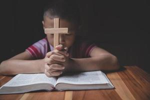 menino com as mãos segurando uma cruz sagrada e orando a Deus foto