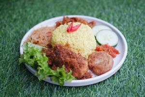 indonésio estilo amarelo arroz com picado frango dentro branco prato em verde Relva fundo foto