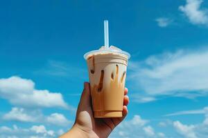 mão segurando gelado café dentro uma plástico copo com uma azul céu e nuvem fundo. ai gerado foto