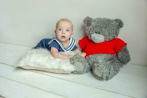 infantil bebê Garoto mentiras em travesseiro com Urso de pelúcia Urso brinquedo em branco quarto fundo foto