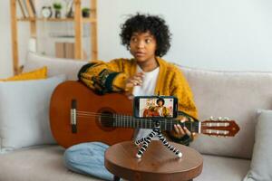 blogueiro guitarrista. africano americano menina blogueiro jogando guitarra falando para Webcam gravação vlog. social meios de comunicação influenciador mulher transmissão às casa dentro de casa. música conteúdo O Criador transmissão tutorial. foto