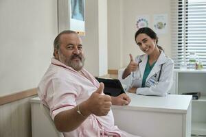 lindo fêmea médico dentro uniforme e branco masculino paciente sorridente e olhando às Câmera, saúde checar compromisso às uma trabalhando mesa, saudável dieta clínica hospital. foto