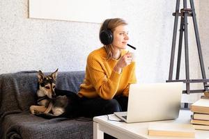mulher com fones de ouvido, estudando on-line, usando um laptop, bebendo café foto
