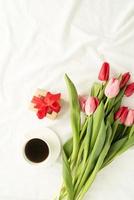 tulipas cor de rosa, xícara de café e vista superior do presente na cama branca