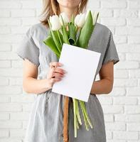 mulher de vestido listrado segurando flores em forma de tulipa branca e um cartão comemorativo foto